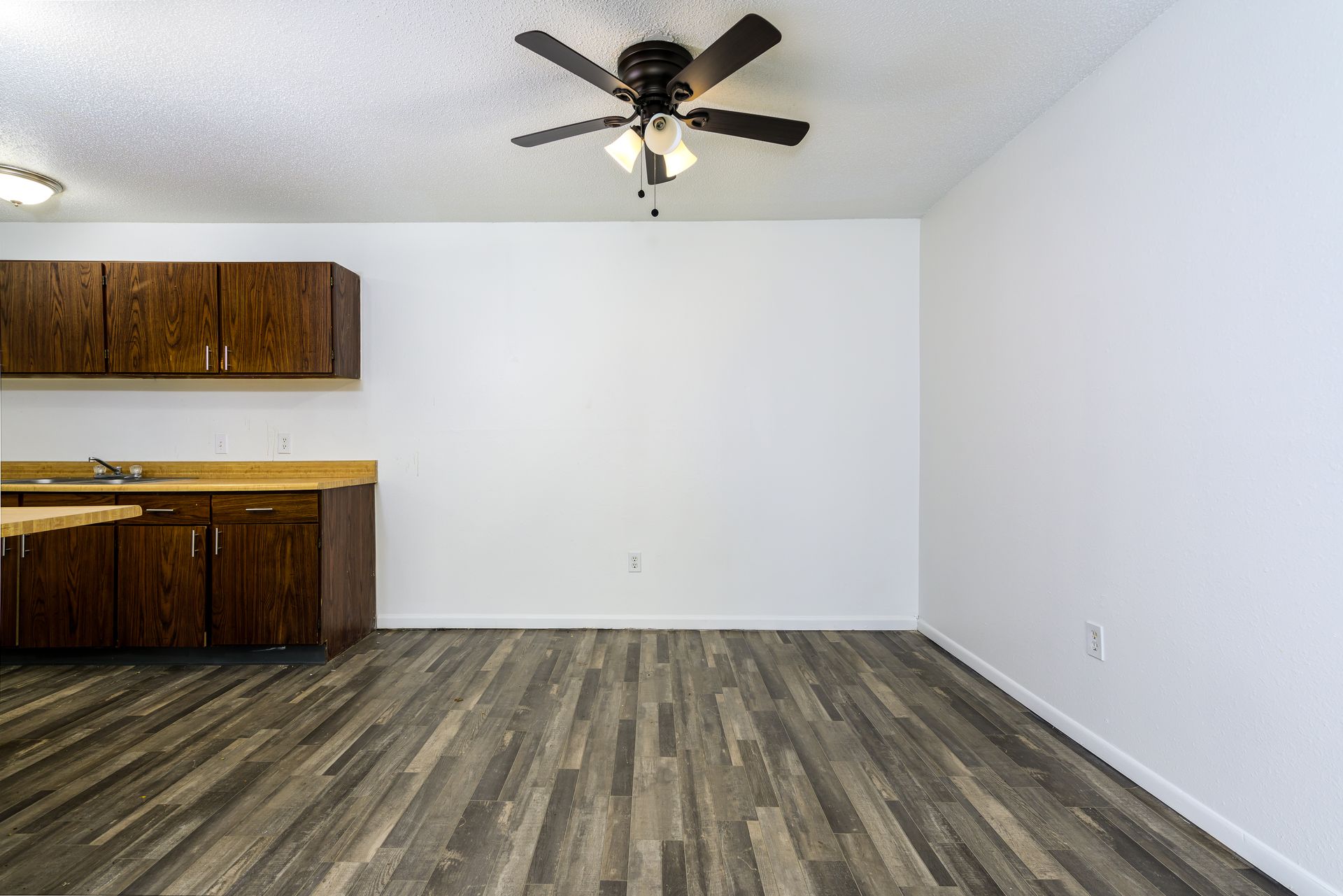 An empty kitchen with a ceiling fan and wooden floors.