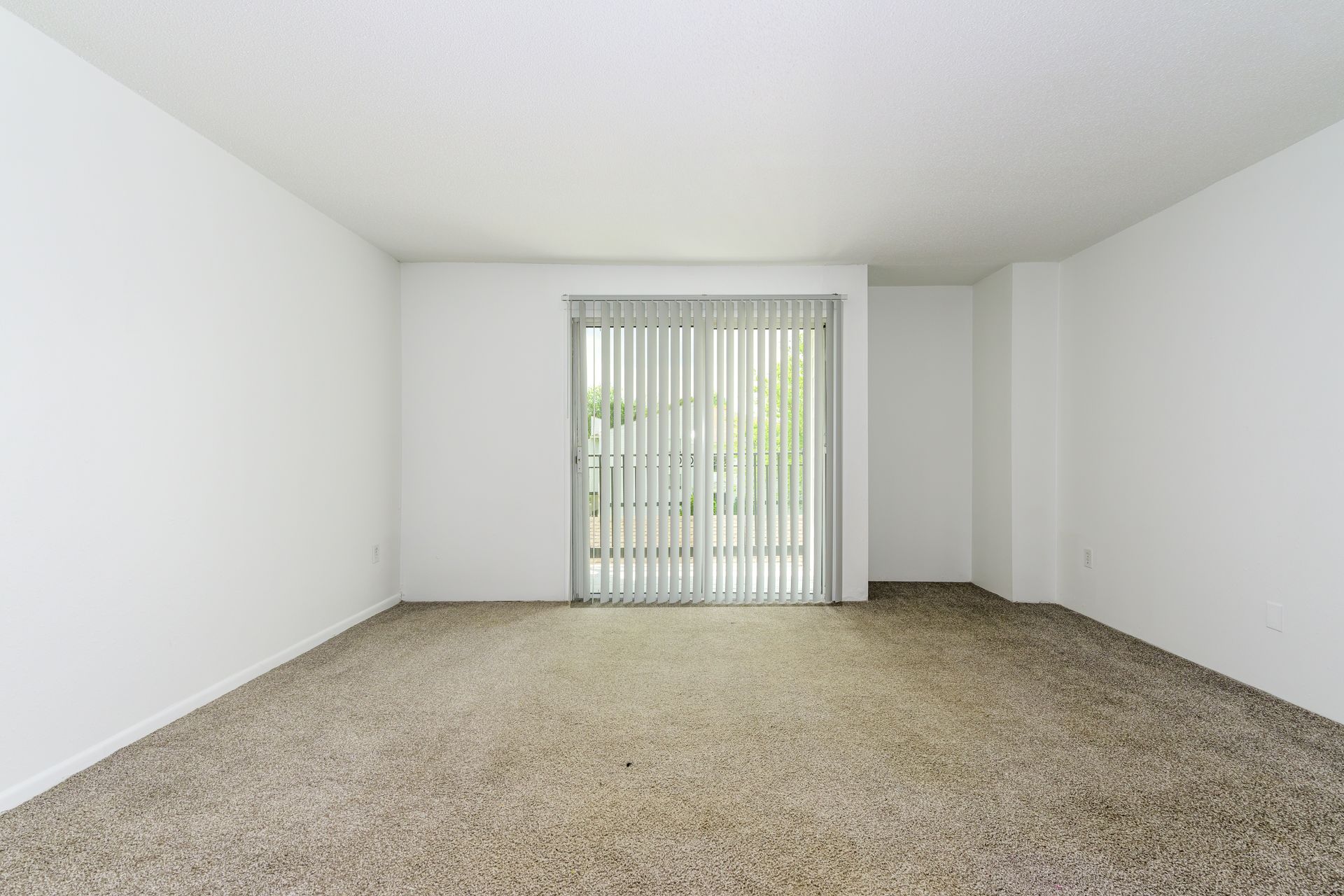 An empty living room with a sliding glass door and carpet.