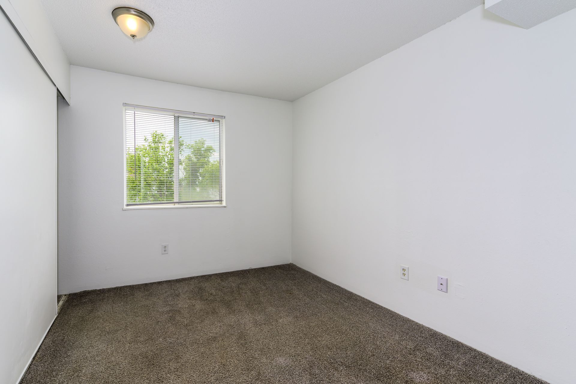 An empty bedroom with a window and a ceiling fan.