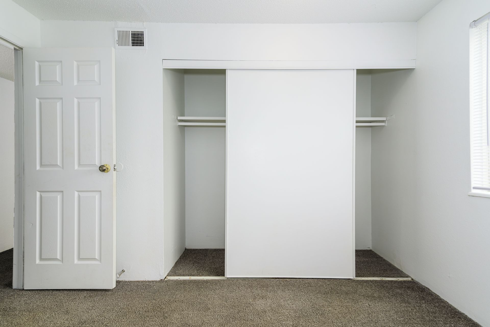 An empty bedroom with two closets and a window.