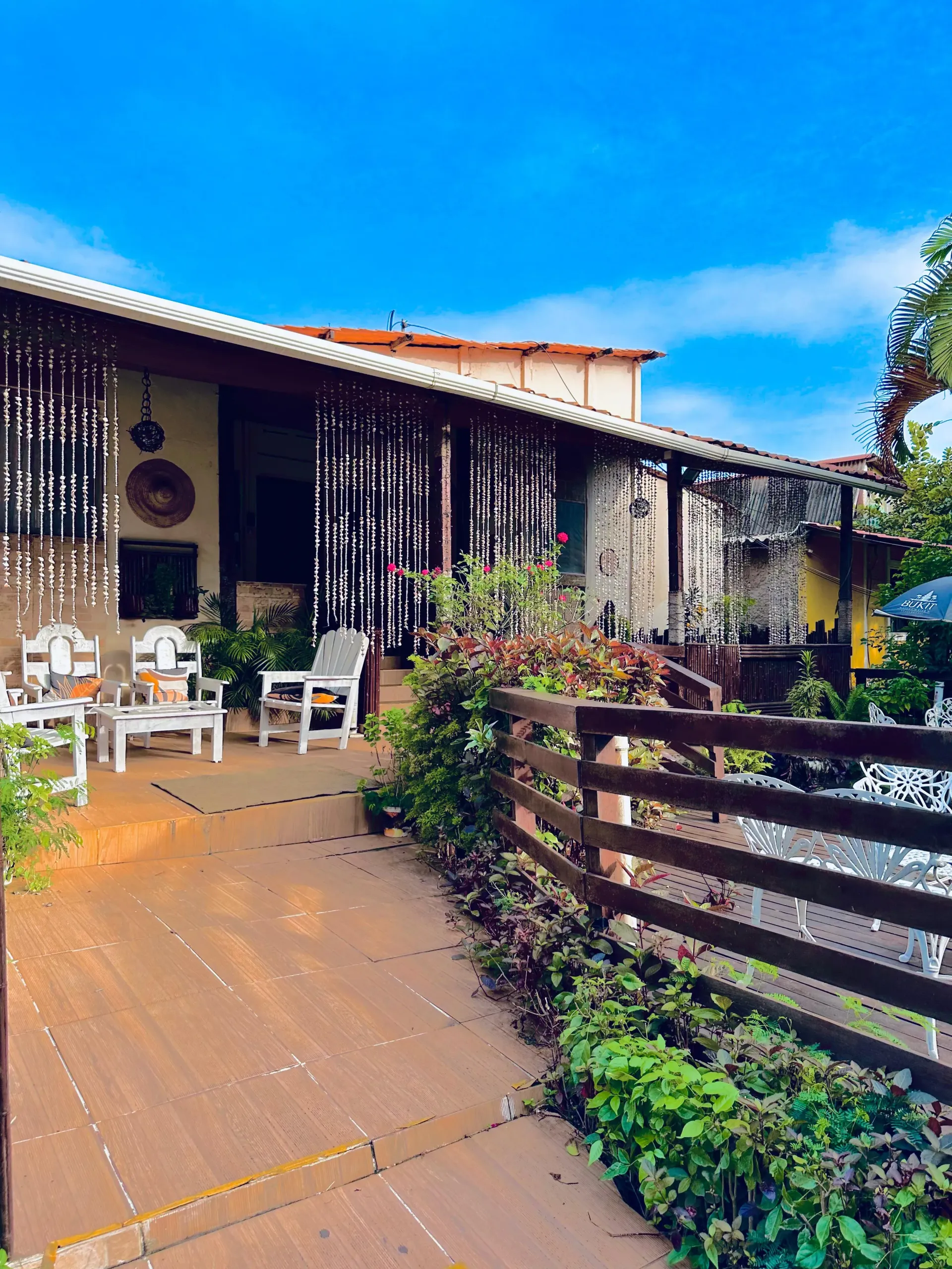 Um pátio com cadeiras, mesas e guarda-sóis em frente a uma casa. Pousada Golfinho Fernando de Noronha