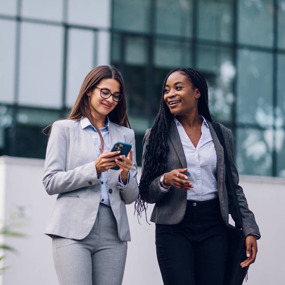 Two women are walking down the street and one is looking at her phone.
