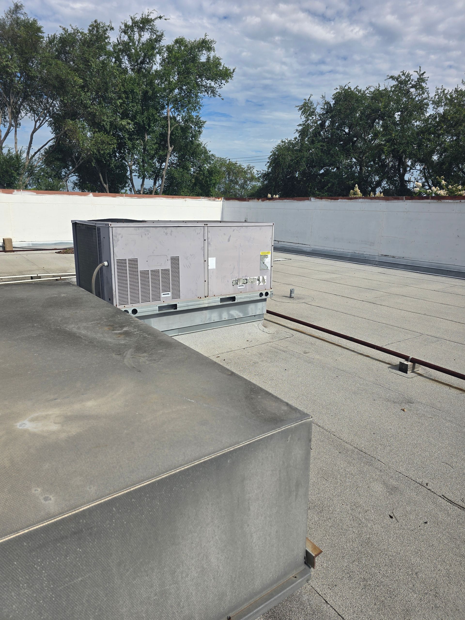 American Air Services, LLC - HVAC unit on a flat roof, trees in the background, sunny day.