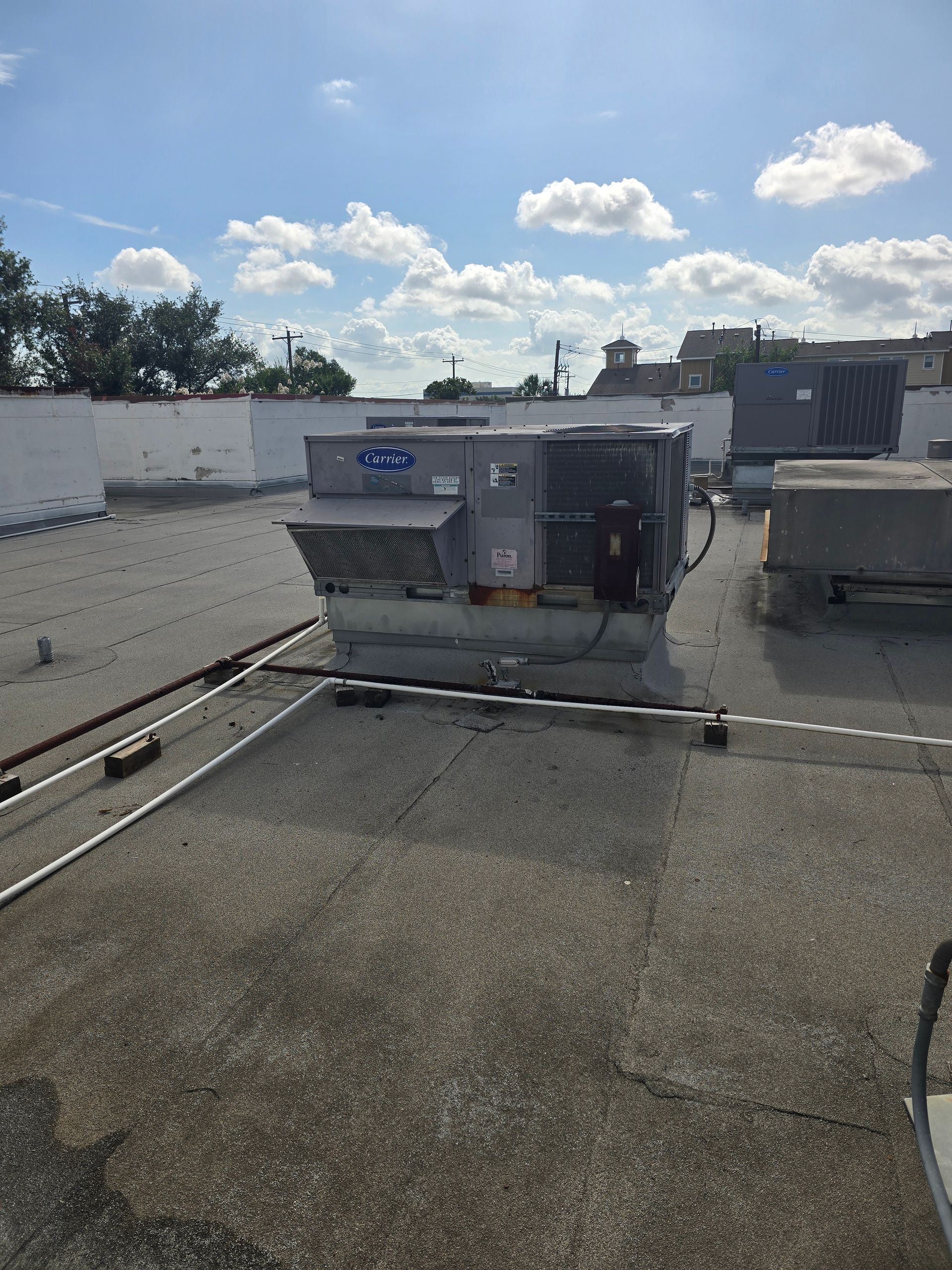American Air Services, LLC - Rooftop with HVAC units on a sunny day; white parapet, blue sky, gray concrete.