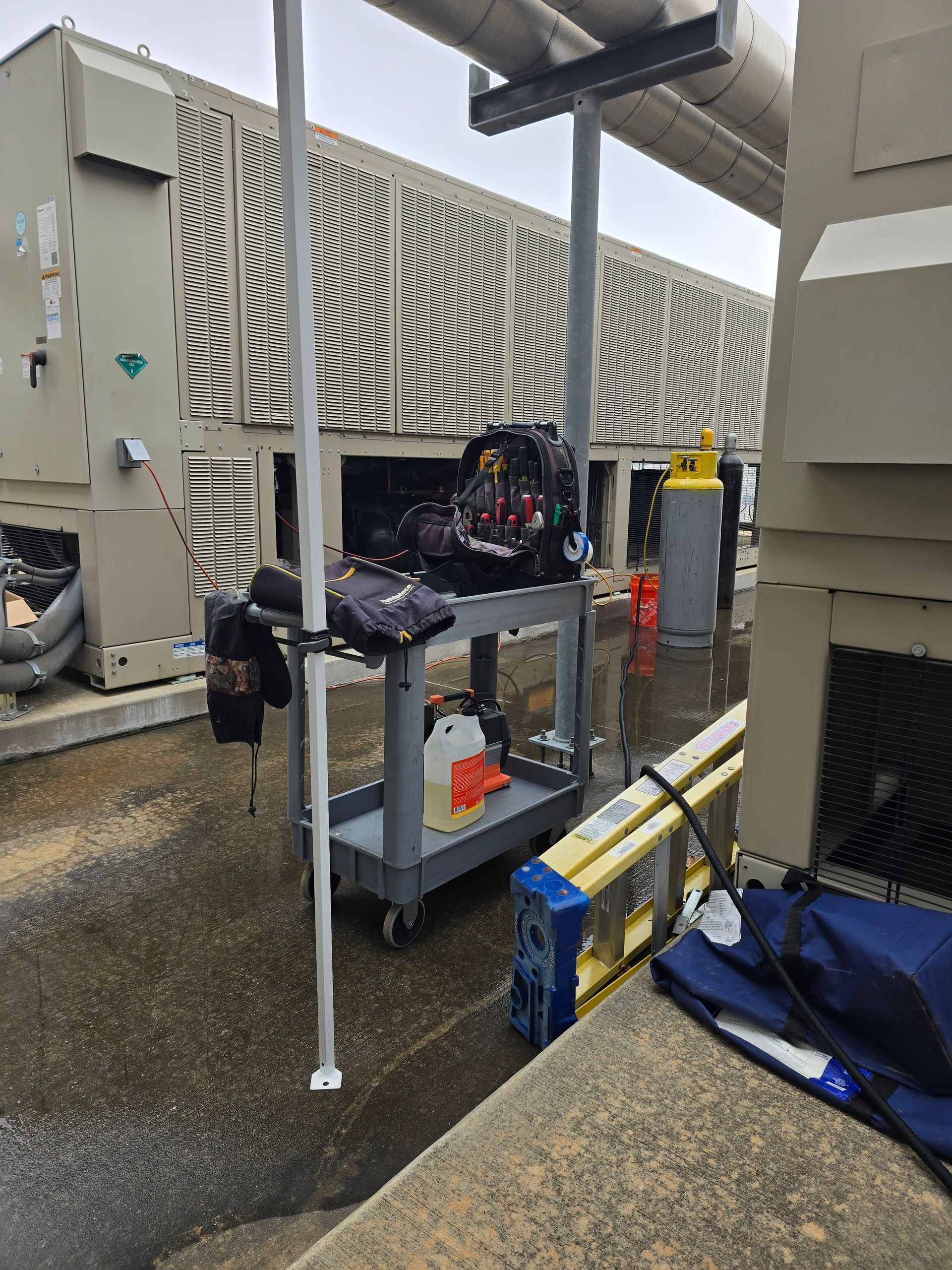 American Air Services, LLC - A rooftop scene with a worker's cart holding tools, a ladder, and HVAC equipment.