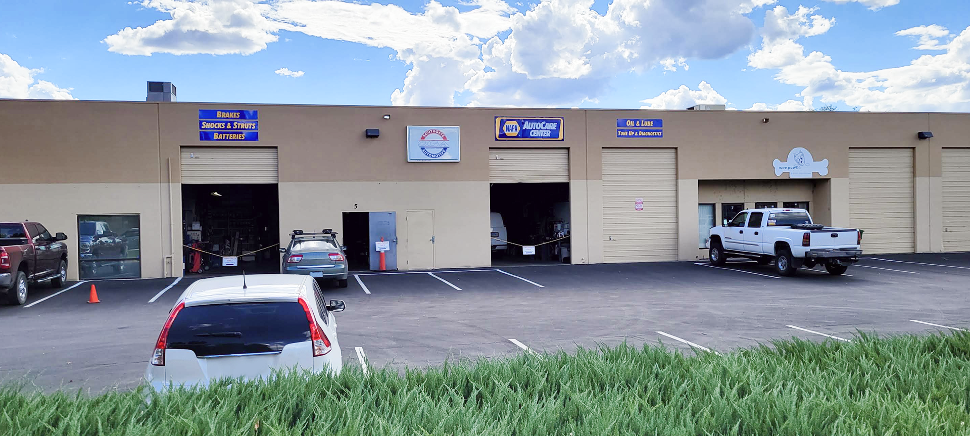 A beige auto repair shop with open garage doors and parked vehicles under a blue sky. | Southgate Automotive