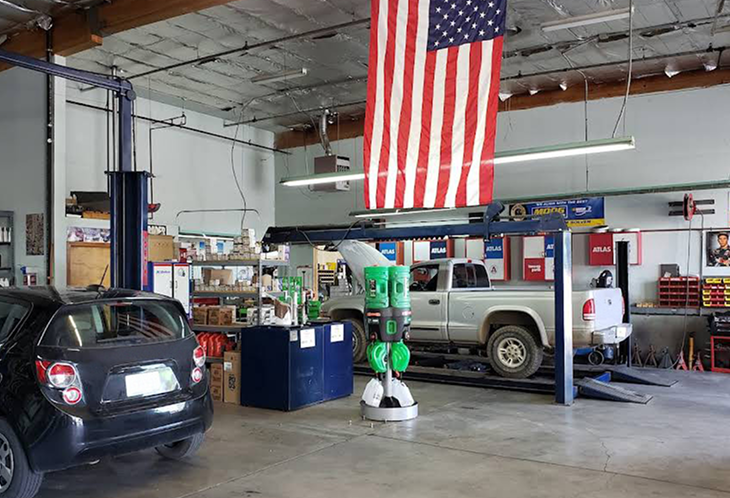 Inside a car repair shop, a truck is on a lift, a black car in front. An American flag hangs from the ceiling. | Southgate Automotive