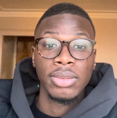 A man wearing glasses and a black hoodie looks at the camera