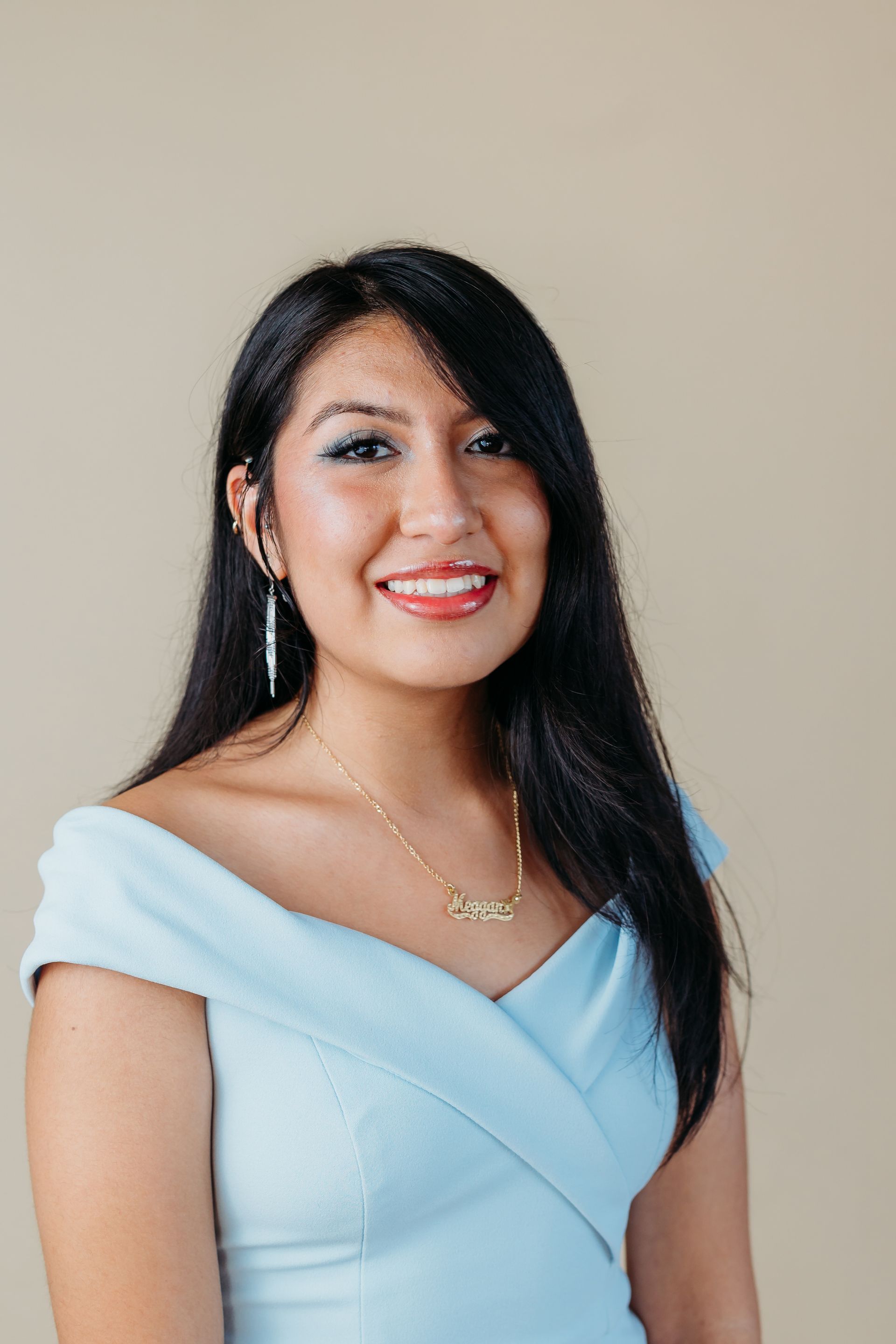 A woman in a light blue dress and necklace is smiling for the camera.