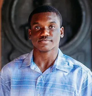 A young man in a blue plaid shirt is looking at the camera.