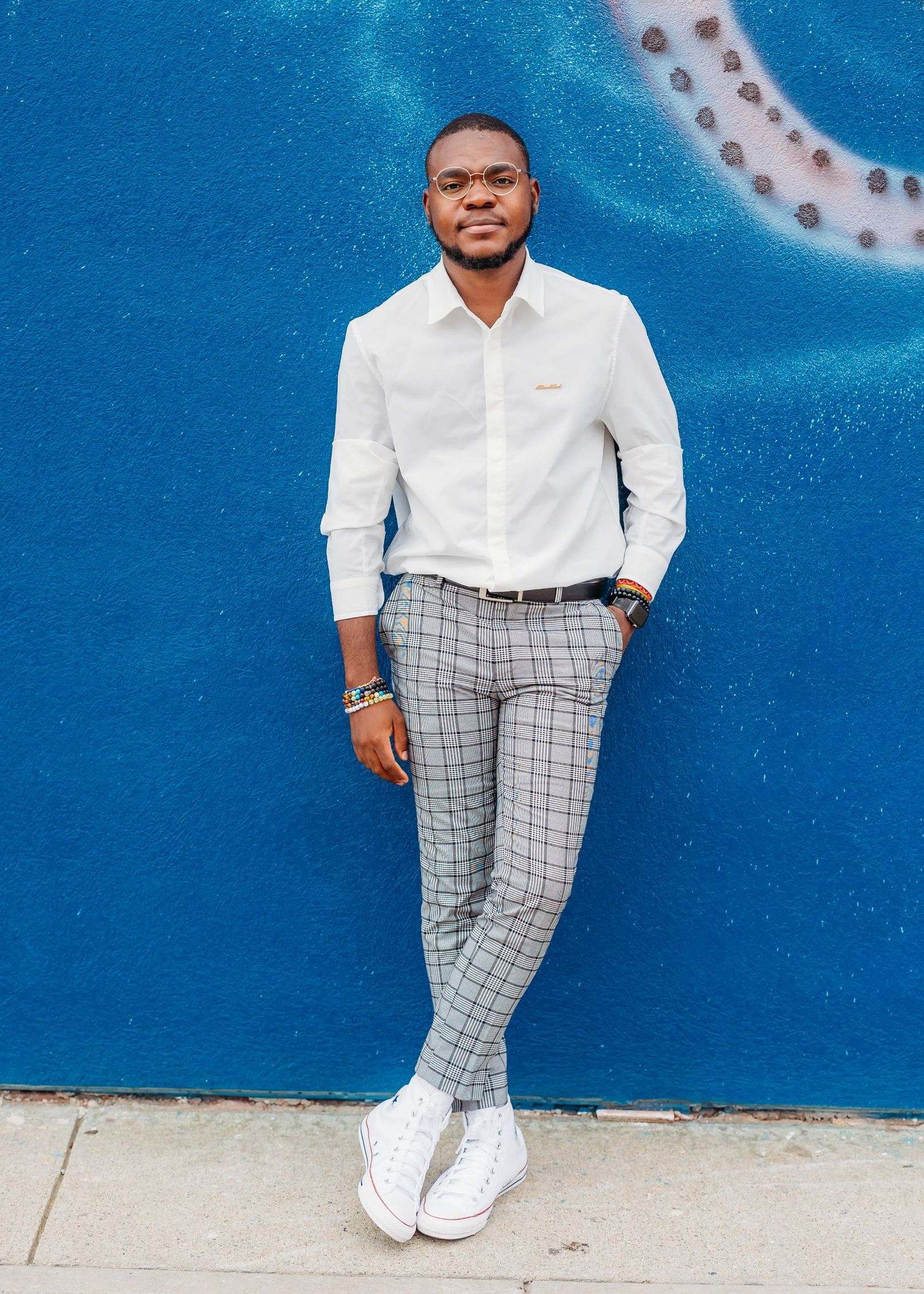 A man in a white shirt and plaid pants is standing in front of a blue wall.