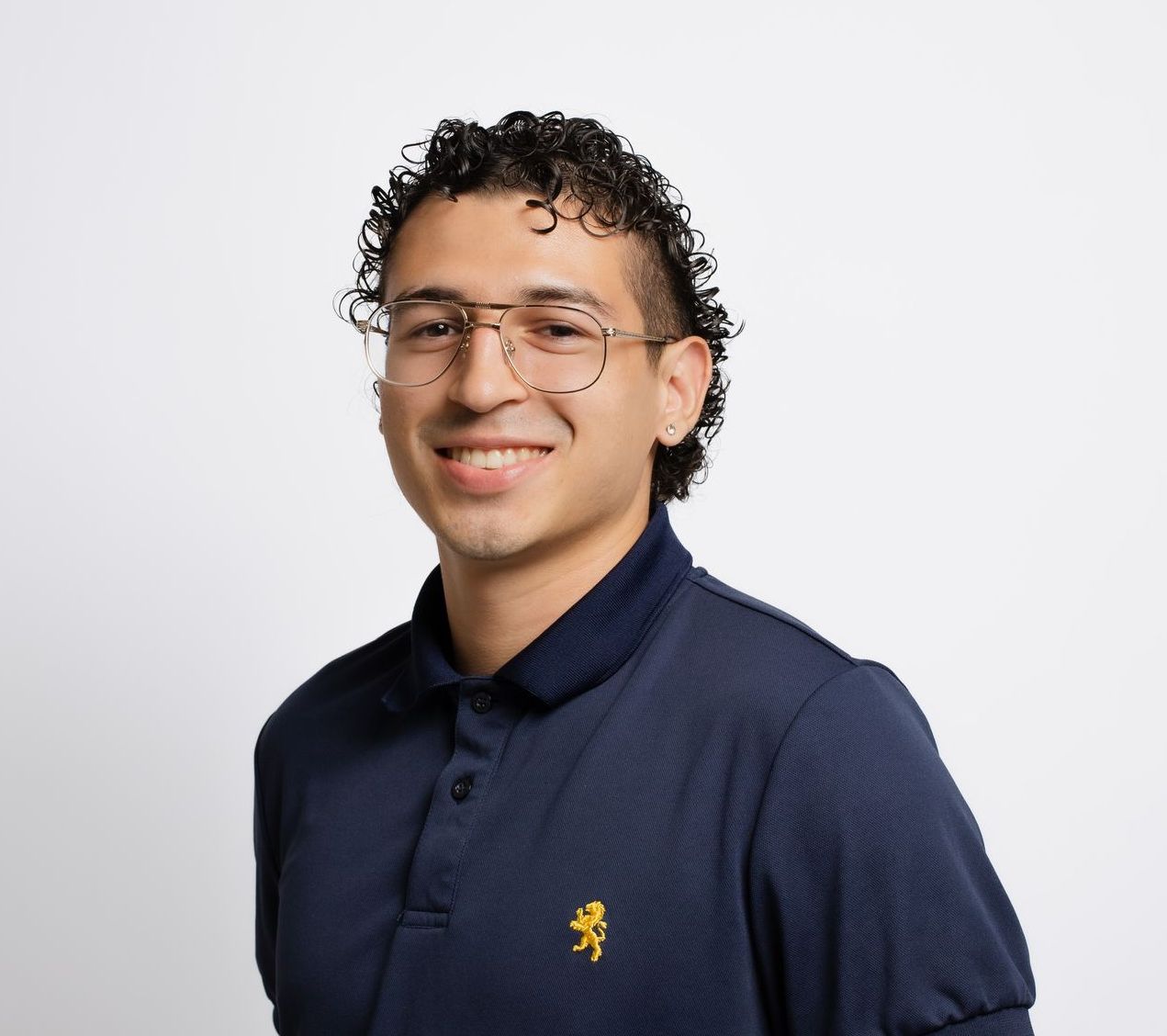 A young man wearing glasses and a blue polo shirt is smiling for the camera.
