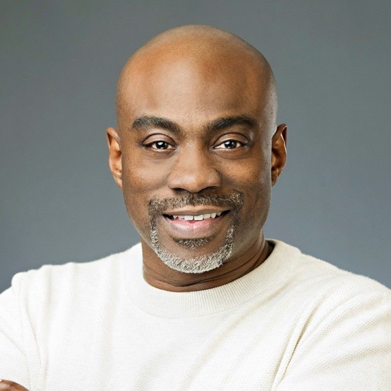 A bald man with a beard is wearing a white sweater and smiling.