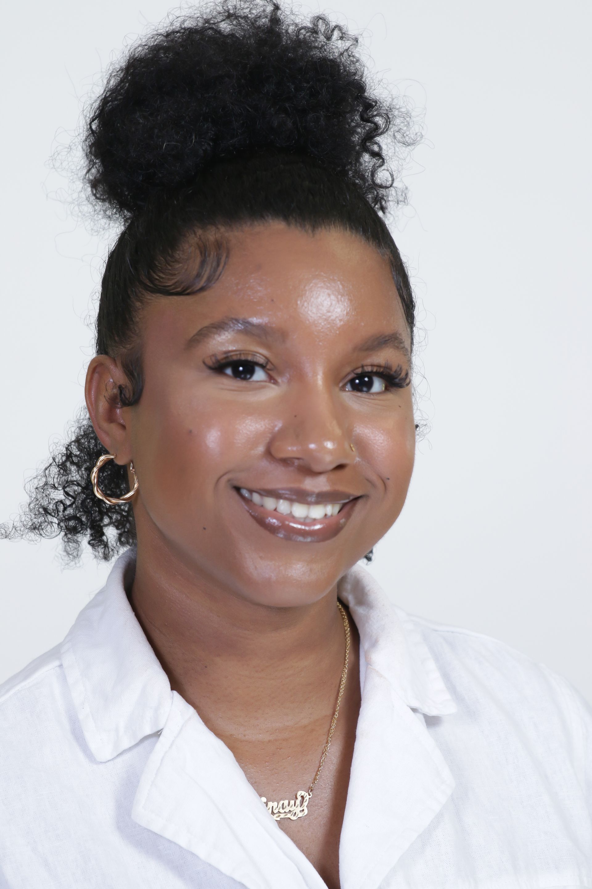 A woman with curly hair is wearing a white lab coat and smiling.
