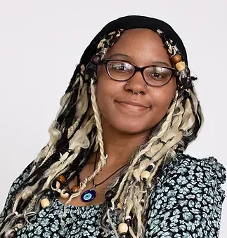 A woman with dreadlocks and glasses is smiling for the camera.