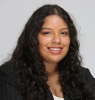 A woman with long curly hair is wearing a black jacket and smiling.