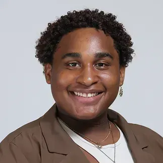 A young man with curly hair and earrings is smiling for the camera.