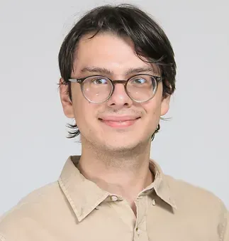 A young man wearing glasses and a tan shirt is smiling for the camera.