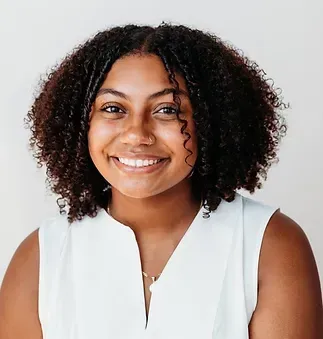 A woman with curly hair is wearing a white shirt and smiling.