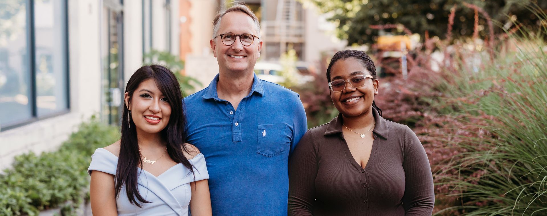 A man and two women are posing for a picture in front of a building.