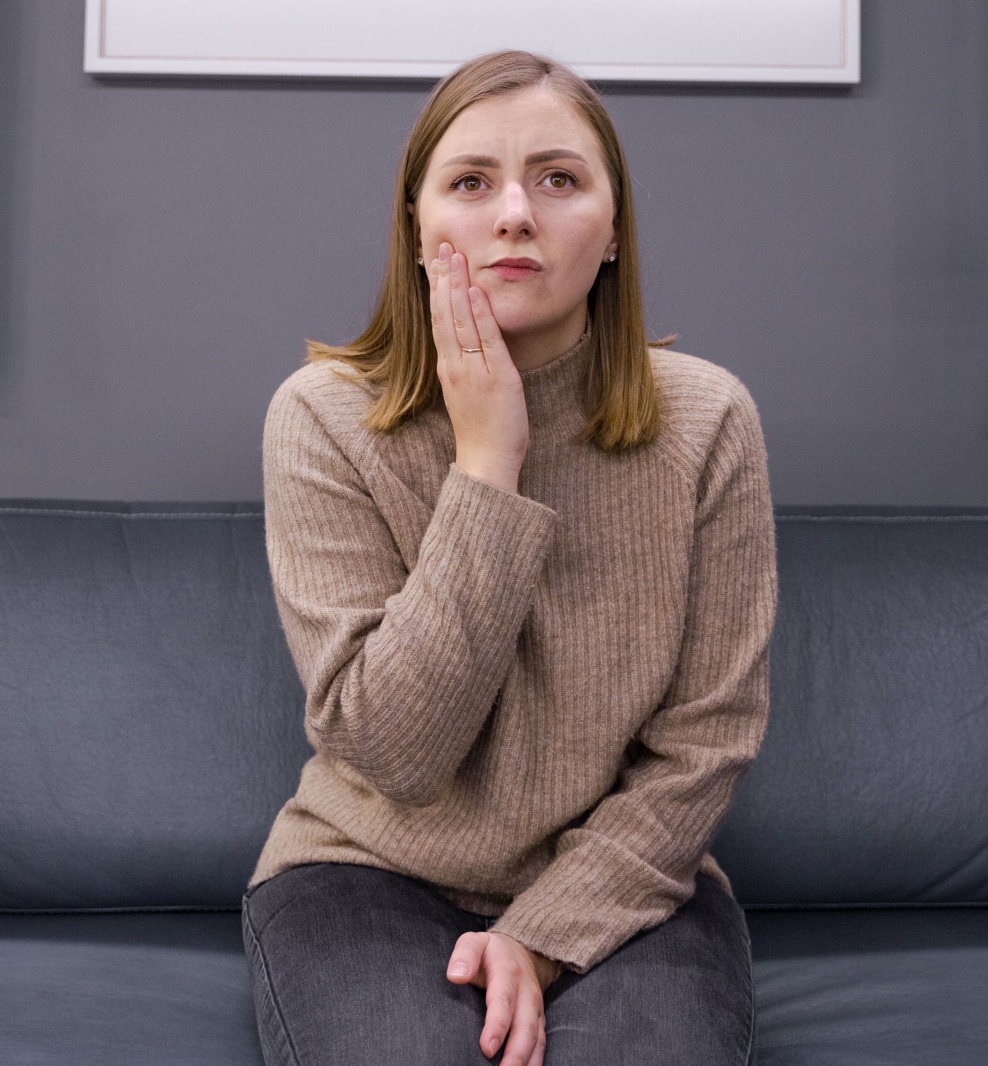 A woman is sitting on a couch with her hand on her face.