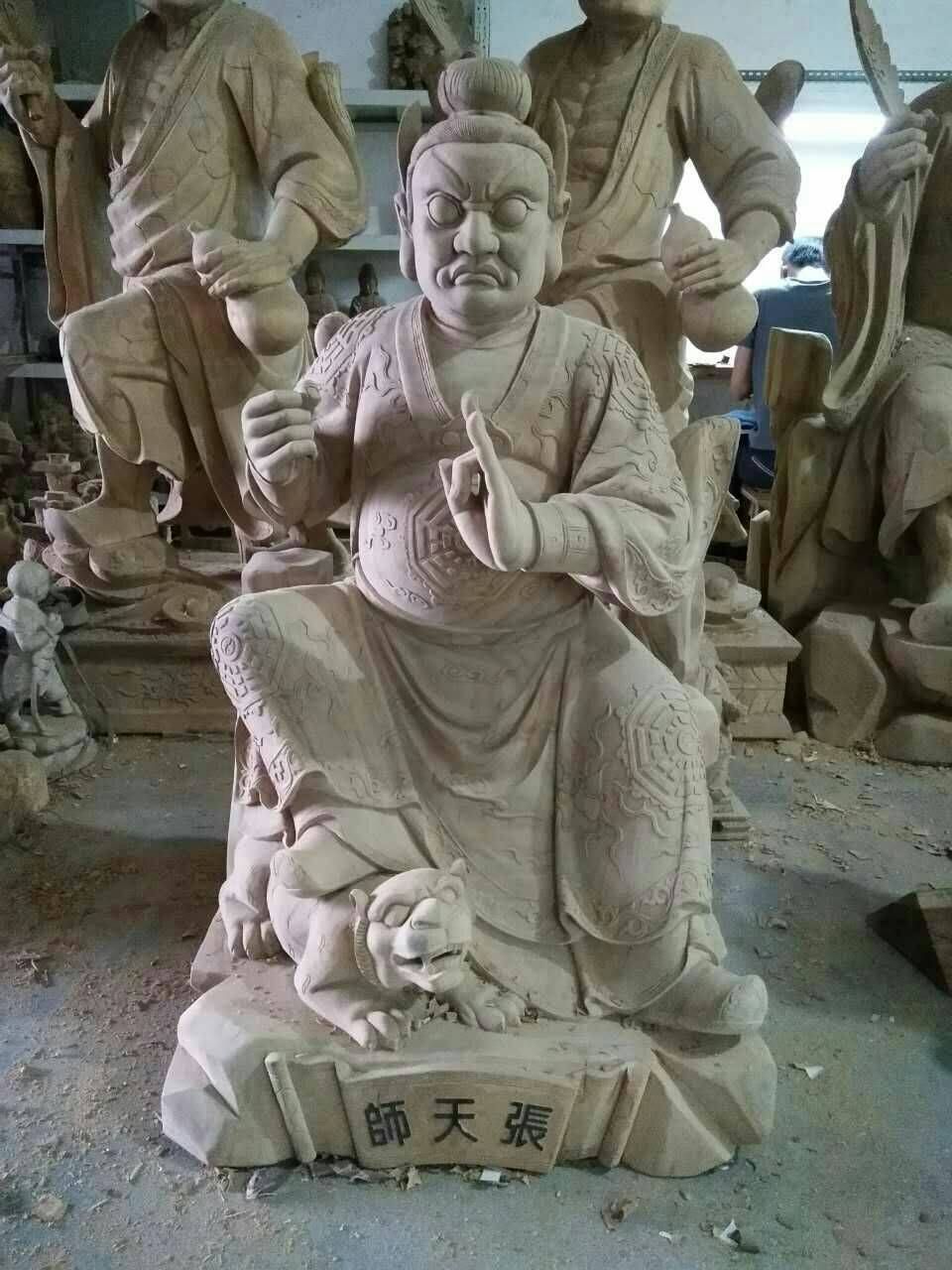 粉紅色石雕神像,神像端坐,手持權杖,底座有老虎,後面還有其他雕像。