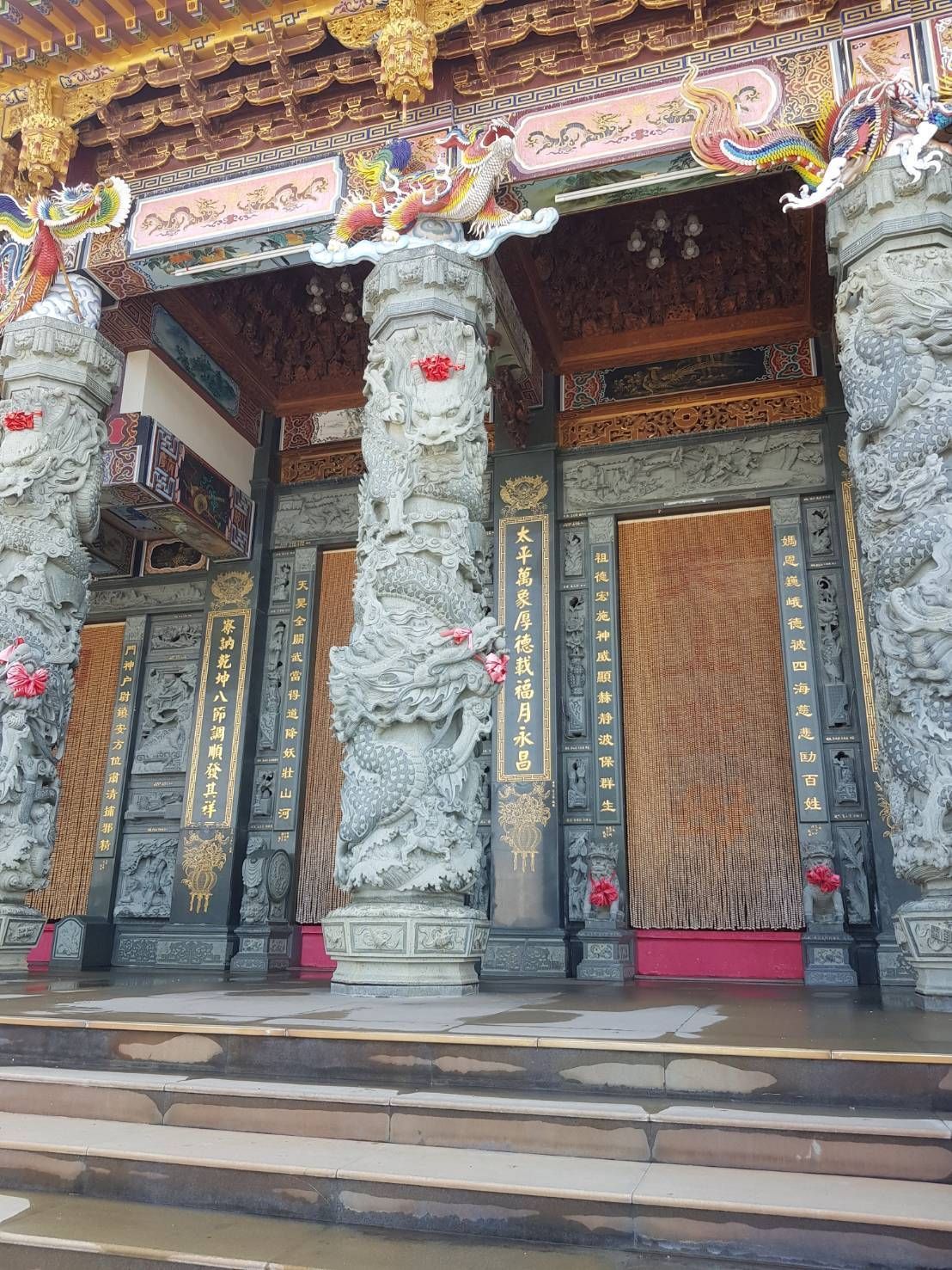 華麗的寺廟入口,有雕刻精美的石柱、金色的屋頂裝飾和寬闊的台階。