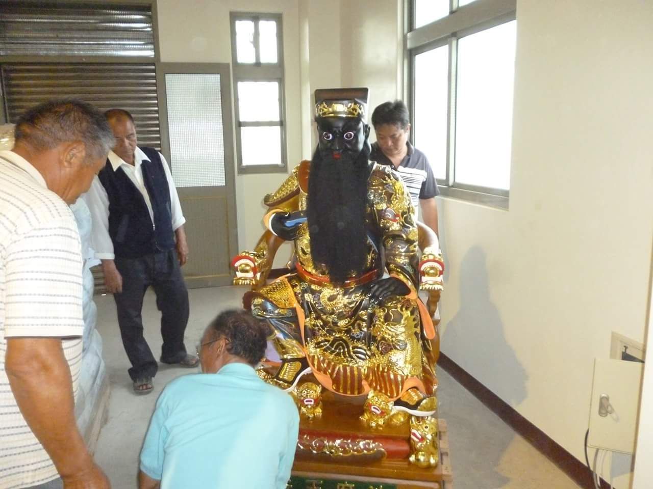 人們在明亮的室內房間裡,對著一尊鍍金的神像祈禱。