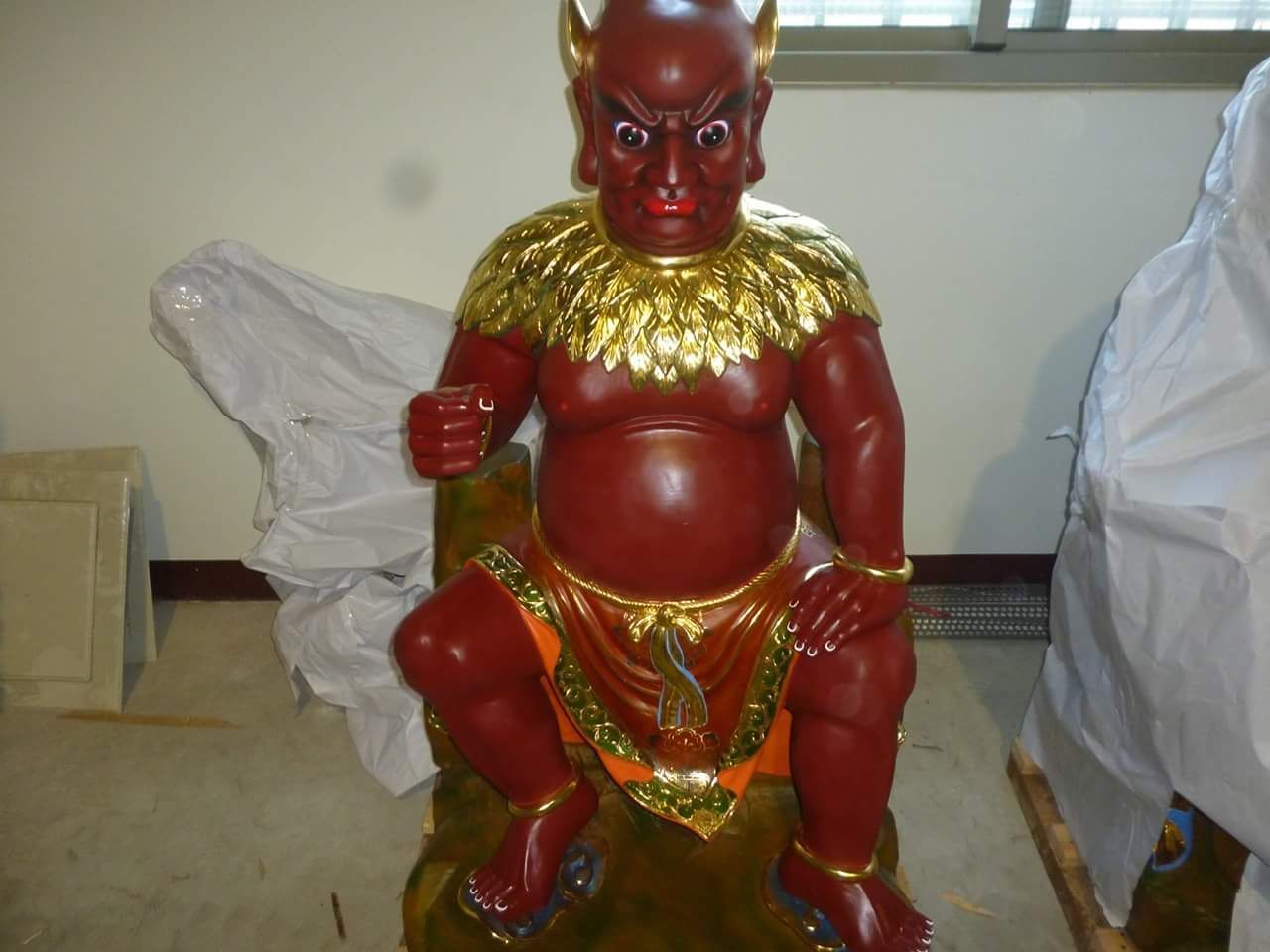 室內地板上擺放著一尊紅色的兒童坐像,雕像邊緣鑲有金邊,戴著珠寶。