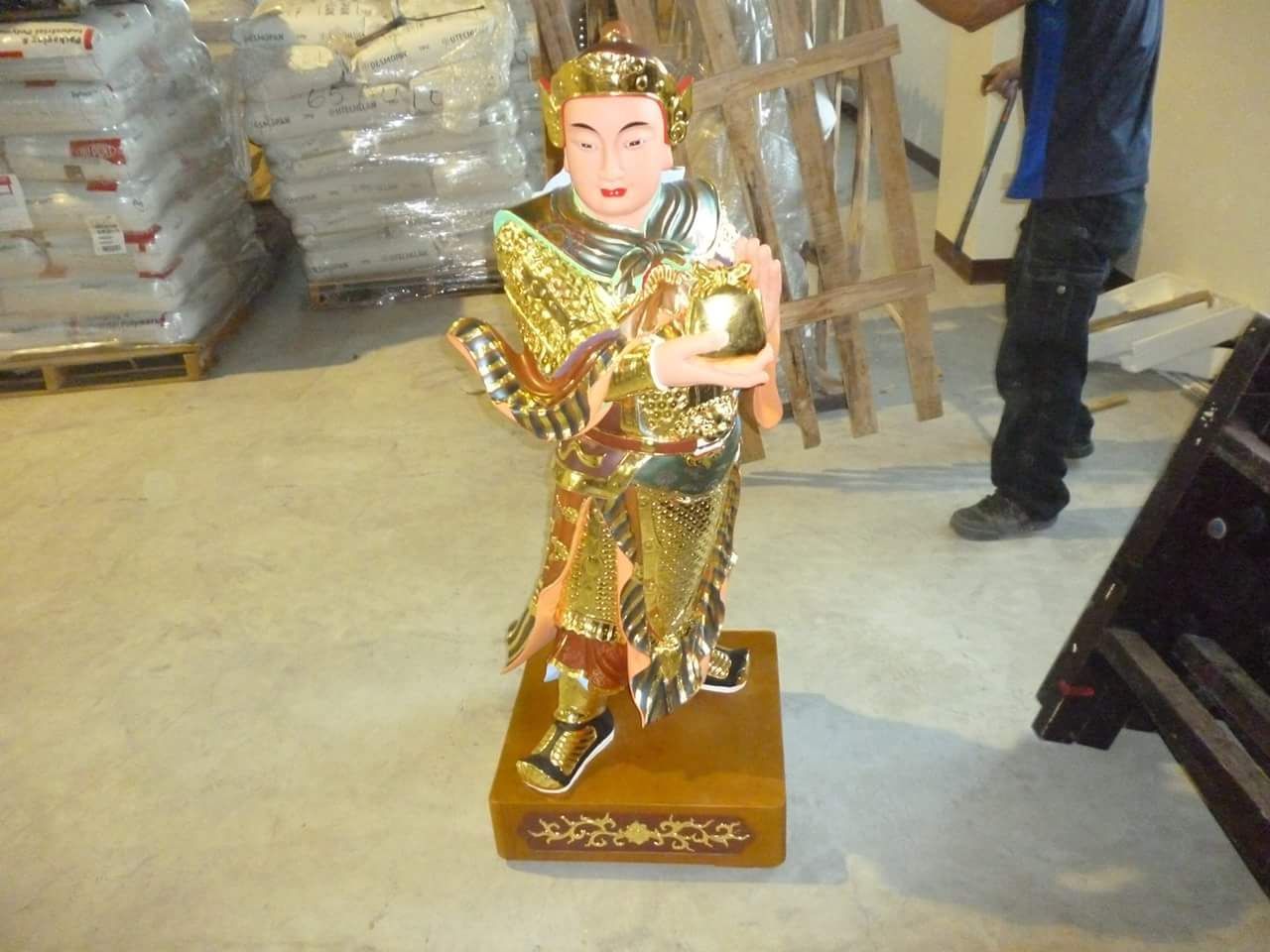 倉庫環境中,一尊金色的、裝飾華麗的兒童音樂家雕像,底座為木質。