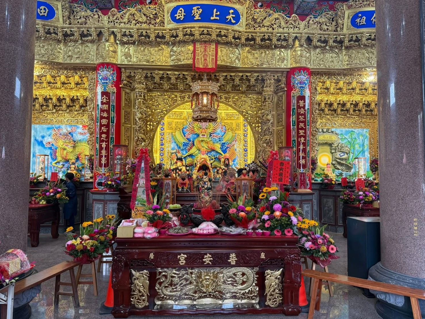 裝飾華麗的寺廟祭壇上擺放著色彩鮮豔的佛像、鮮花,金色華蓋下懸掛著紅色的幡旗。