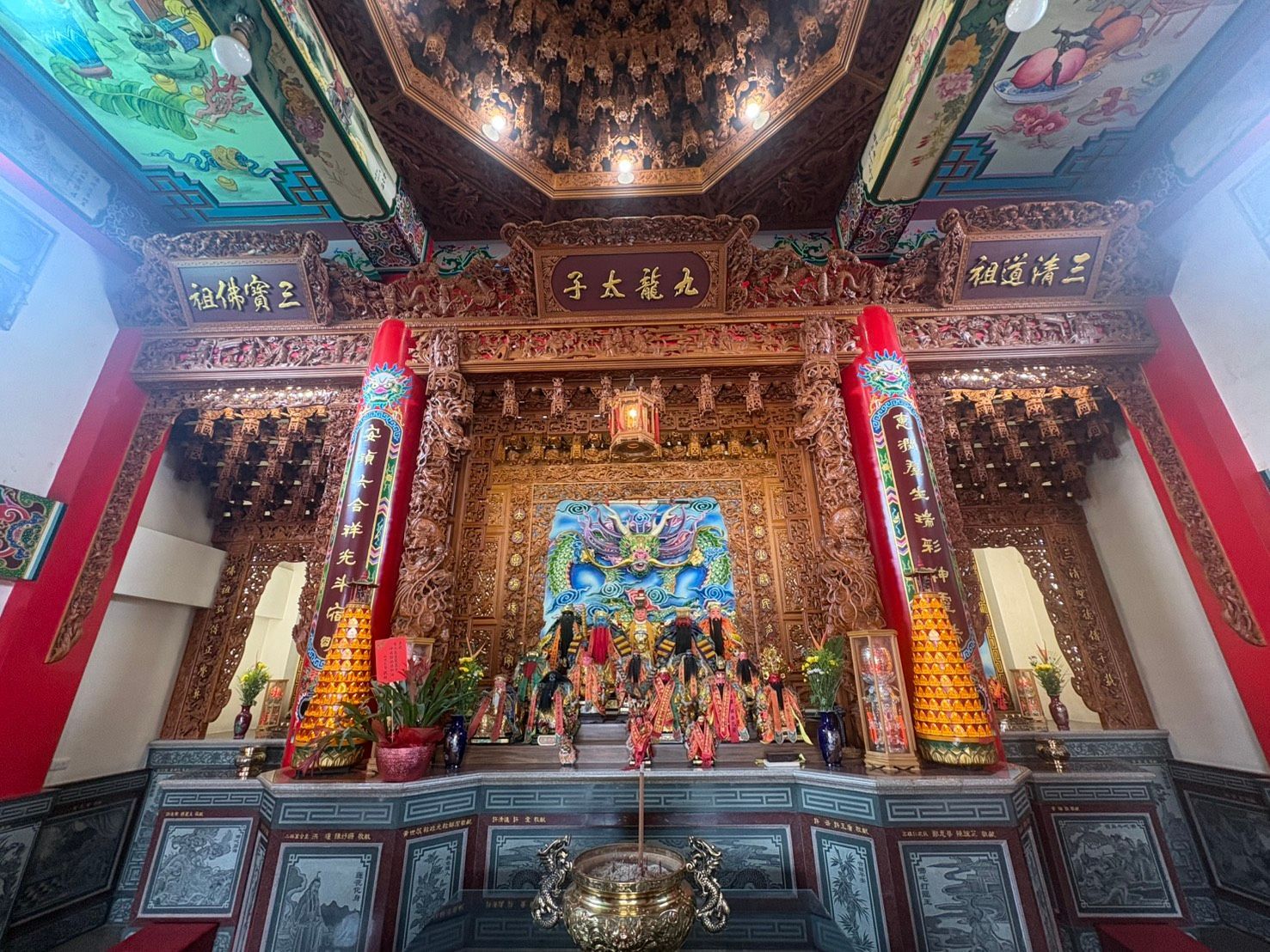華麗的中國寺廟祭壇,紅色的柱子,金色的雕刻,色彩斑斕的神像,上方是裝飾精美的天花板。