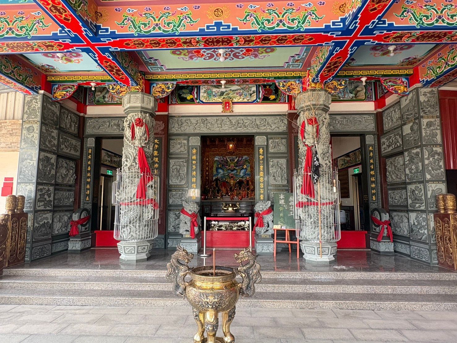 色彩繽紛的寺廟入口,飾有精美的雕花柱子、紅色裝飾,門前還有一個青銅香爐。