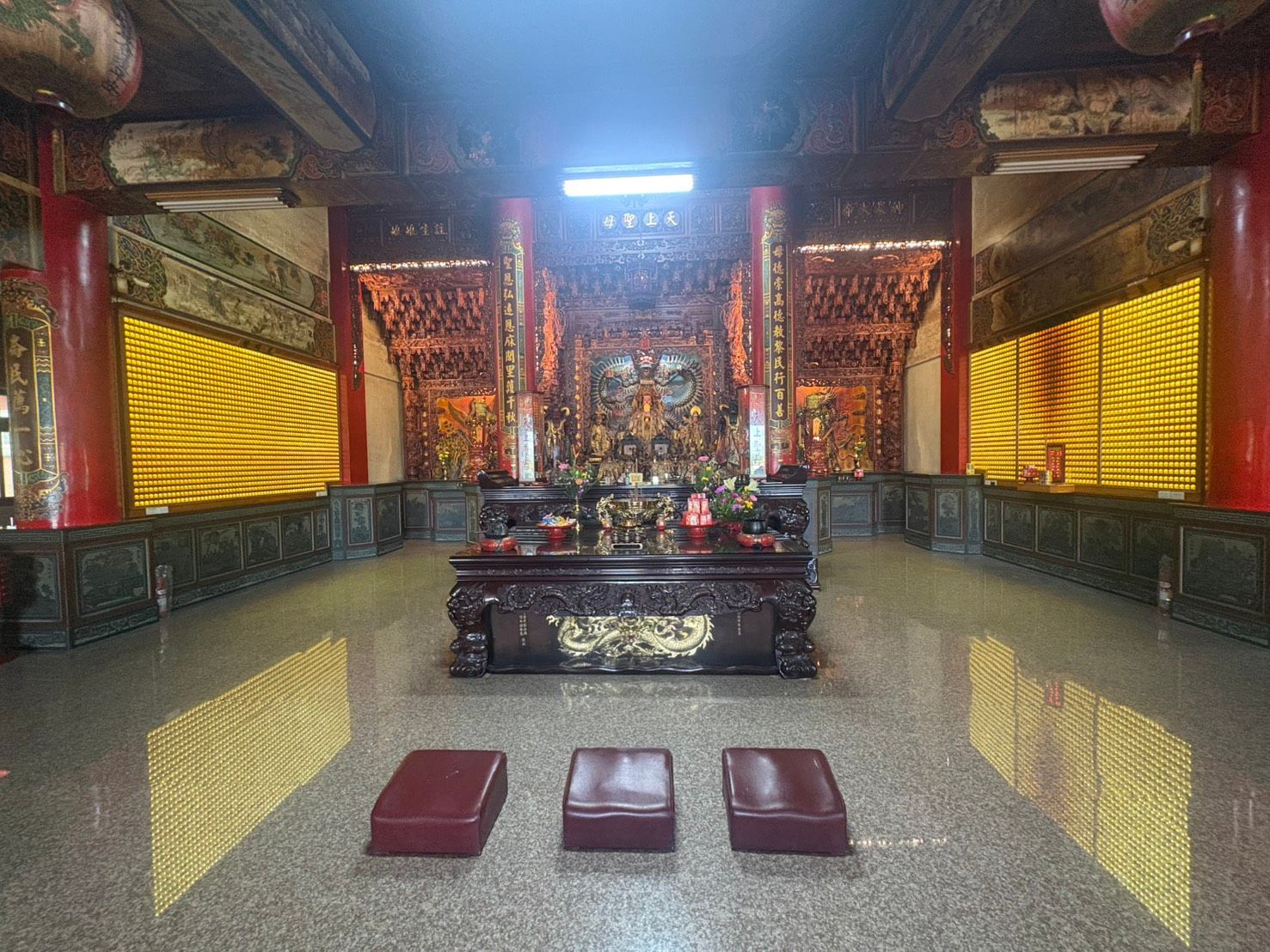 裝飾華麗的寺廟內部,設有紅色祭壇、金色牆壁,以及放置在反光地板上的三個墊子。