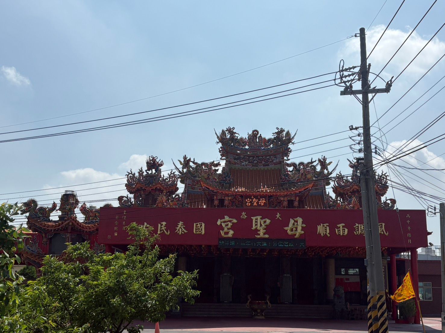 紅色的寺廟外牆上鎘刻著金色的漢字,樹木蔥鬱,電線桿矗立在湛藍的天空下。