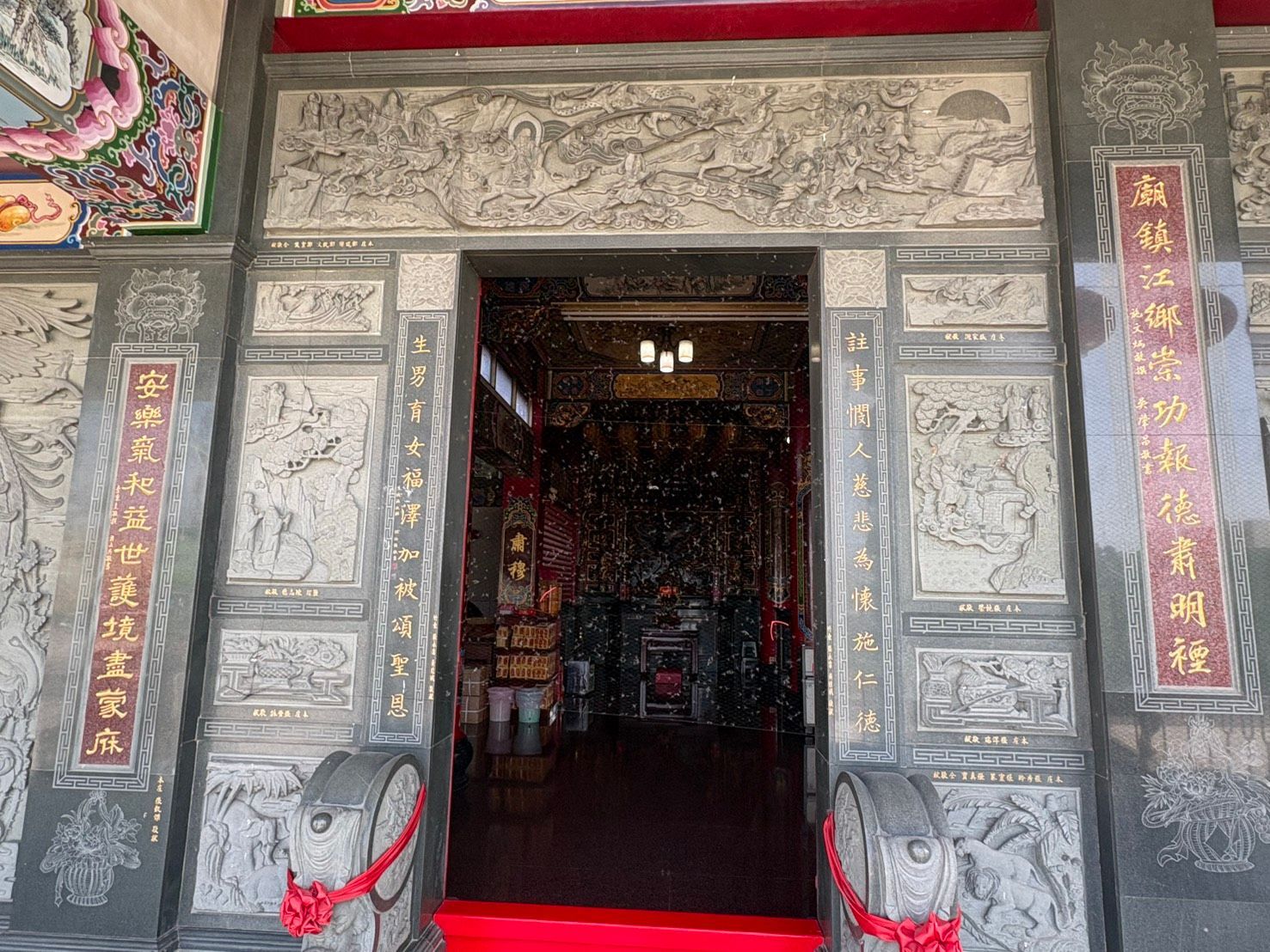 從外面望去,可以看到一座石砌寺廟入口,灰色的石柱上雕刻著圖案,飾以紅色邊框和中文標牌,裡面是一間昏暗的大廳。