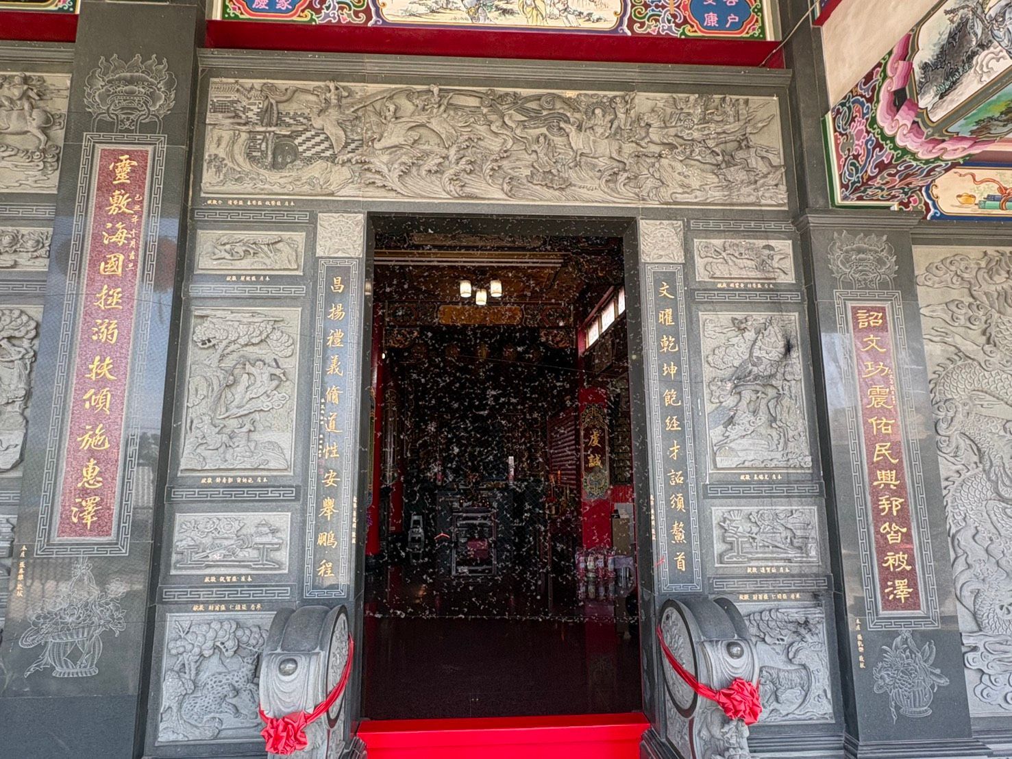 寺廟入口裝飾華麗,灰色石門上雕刻著精美的圖案,紅色的柱子矗立其間,台階上橫跨著紅色的緞帶屏障。