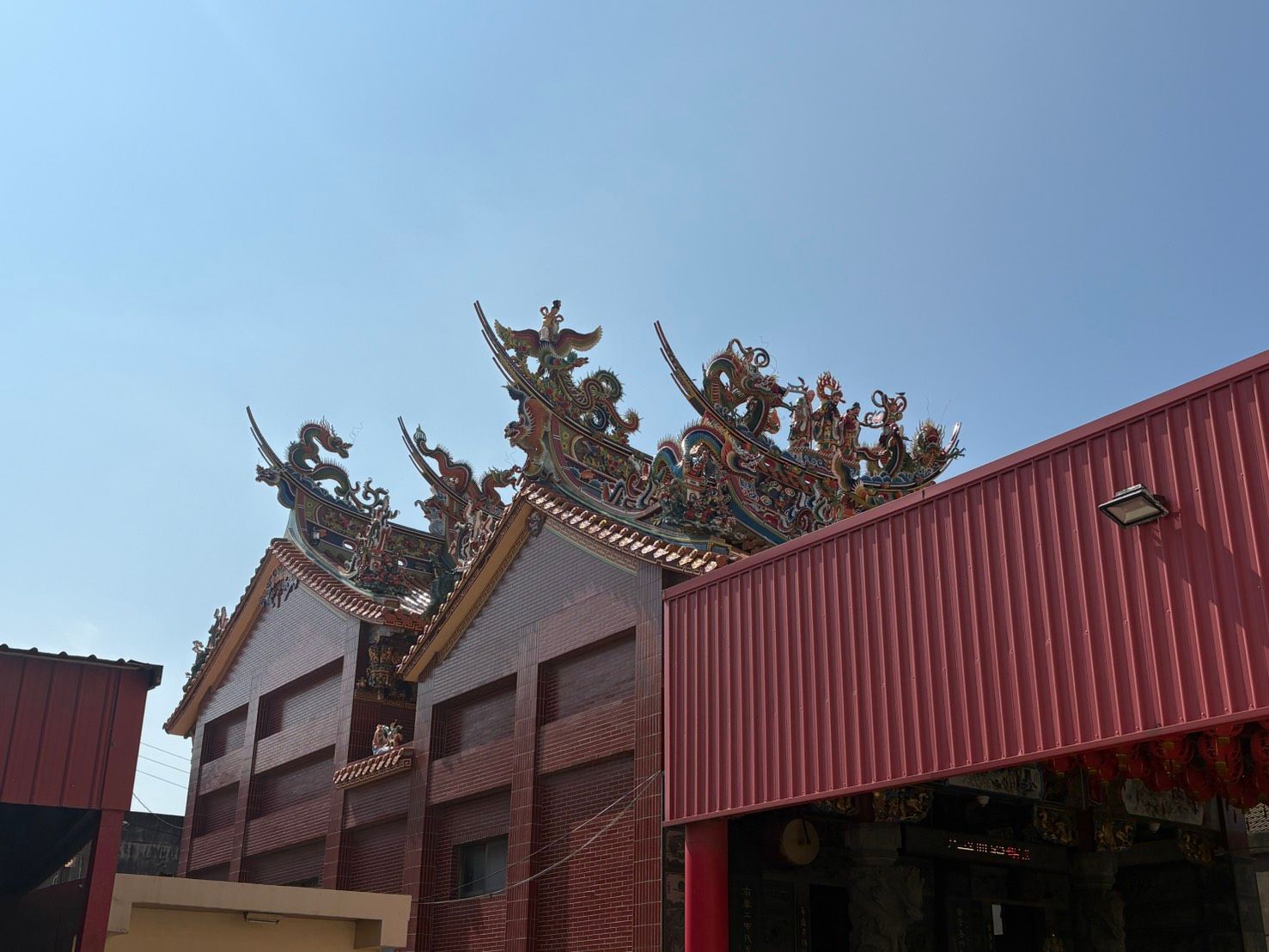 藍天下,傳統寺廟的屋頂上,紅色波紋屋頂後方,雕刻著精美的龍紋。