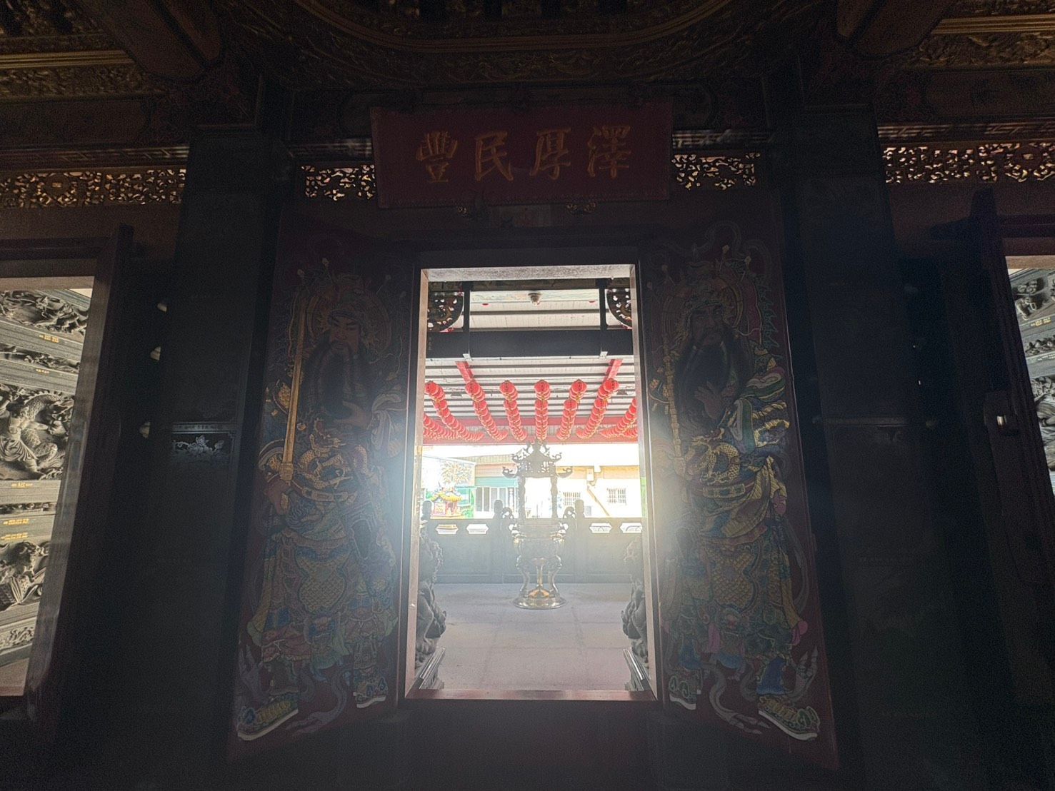 昏暗的寺廟門口框出一個明亮的庭院,庭院外掛著紅燈籠。