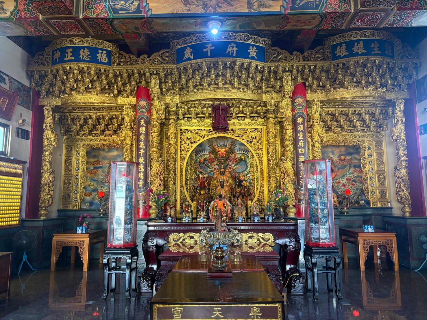 一座裝飾華麗的寺廟神龕內,供奉著金碧輝煌的祭壇,祭壇上擺放著雕像、蠟燭和紅色柱子。