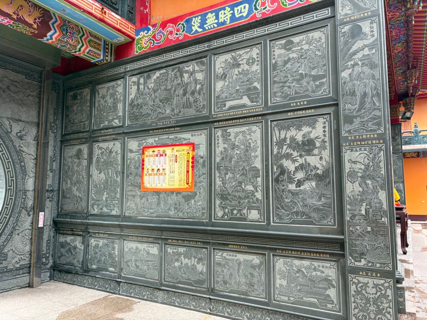 綠色雕花牆上掛著一塊小小的告示牌,位於色彩繽紛的寺廟屋簷下。