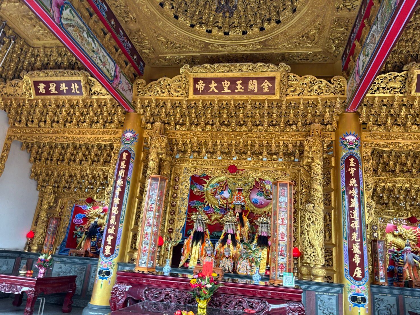 裝飾華麗的金色寺廟祭壇,上面擺放著色彩鮮豔的神像和懸掛的書法牌匾。