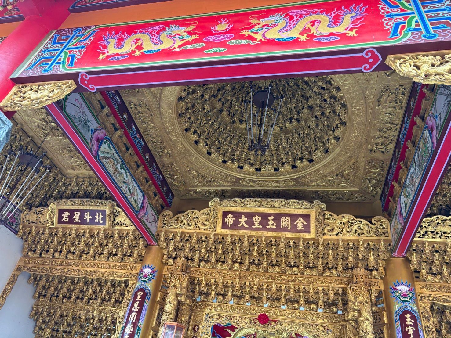 寺廟天花板裝飾華麗,飾以金色雕刻,橫梁色彩斑斕,紅色牌匾上錒刻著漢字。