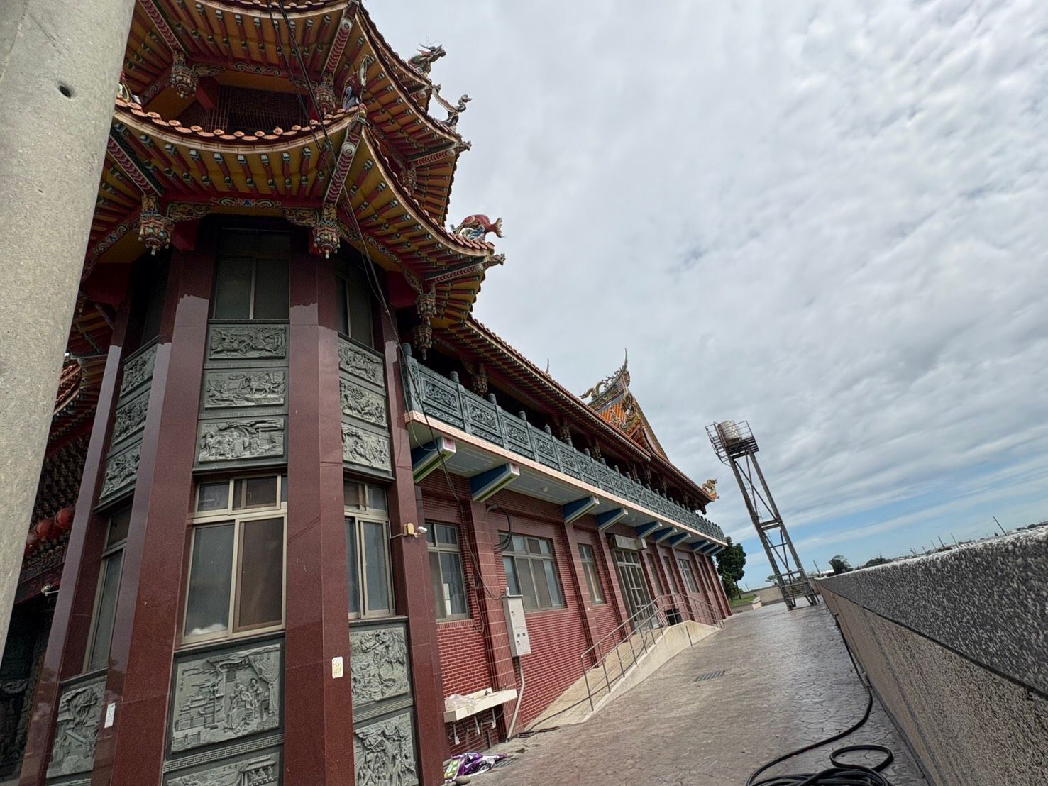在陰雲密佈的天空下,沿著屋頂走道望去,可以看到裝飾華麗的寺廟正面,紅色的柱子和雕刻精美的屋頂。