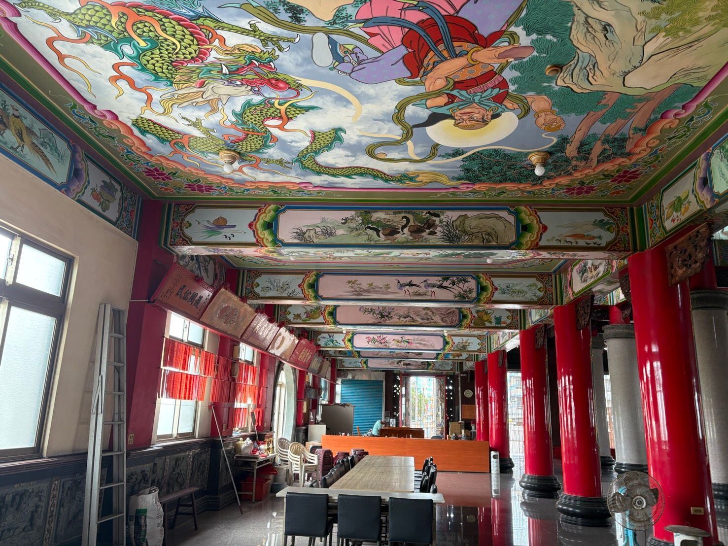 裝飾華麗的寺廟大廳,有紅色的柱子、彩繪的天花板壁畫和一排排的長凳。
