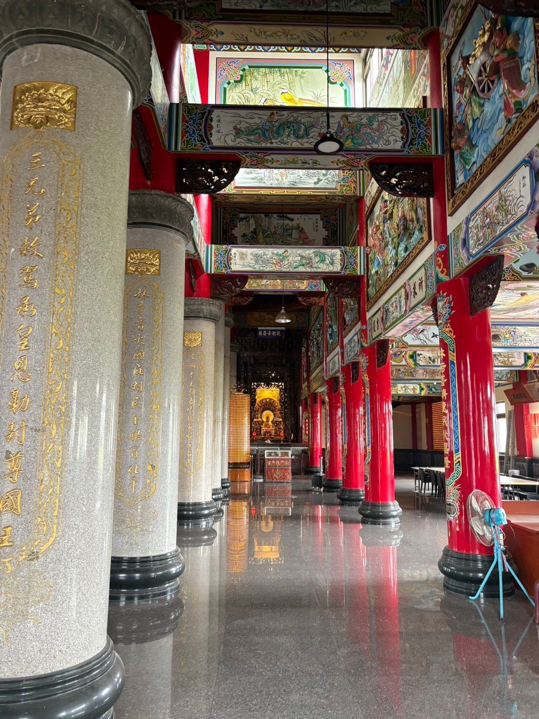 裝飾華麗的寺廟走廊,配有紅色立柱、雕刻壁畫和光潔的反光地板。