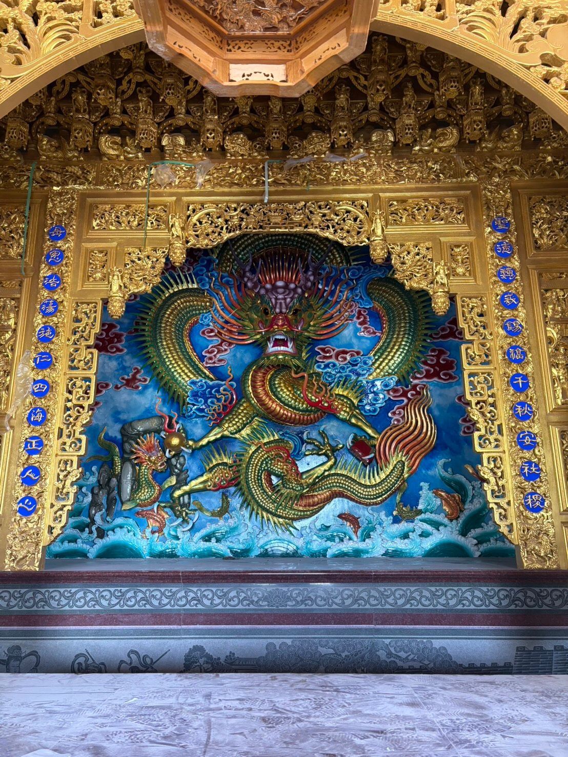 裝飾華麗的寺廟牆壁上,一幅鑲有金框的精美壁畫描繪了一條色彩斑斕的巨龍,周圍環繞著藍色波浪和花卉圖案。