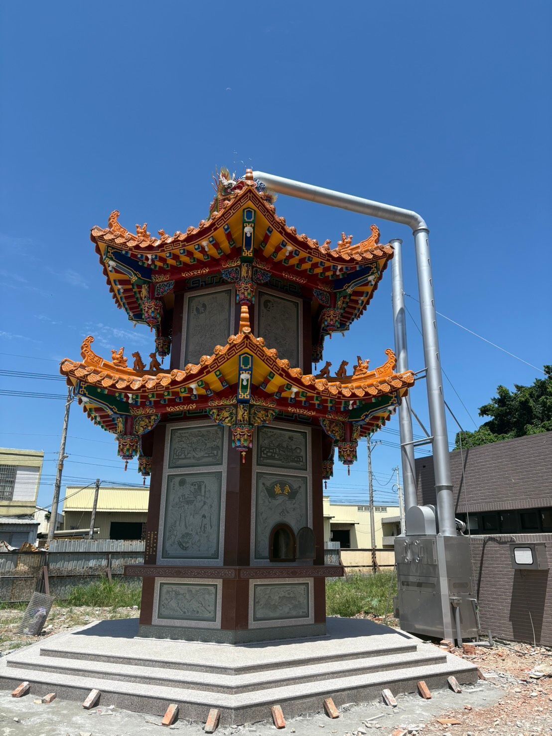 一座裝飾華麗的中式寺廟亭閣,屋頂紅、金、綠三色相間,坐落於藍天下的小型水泥平台上。