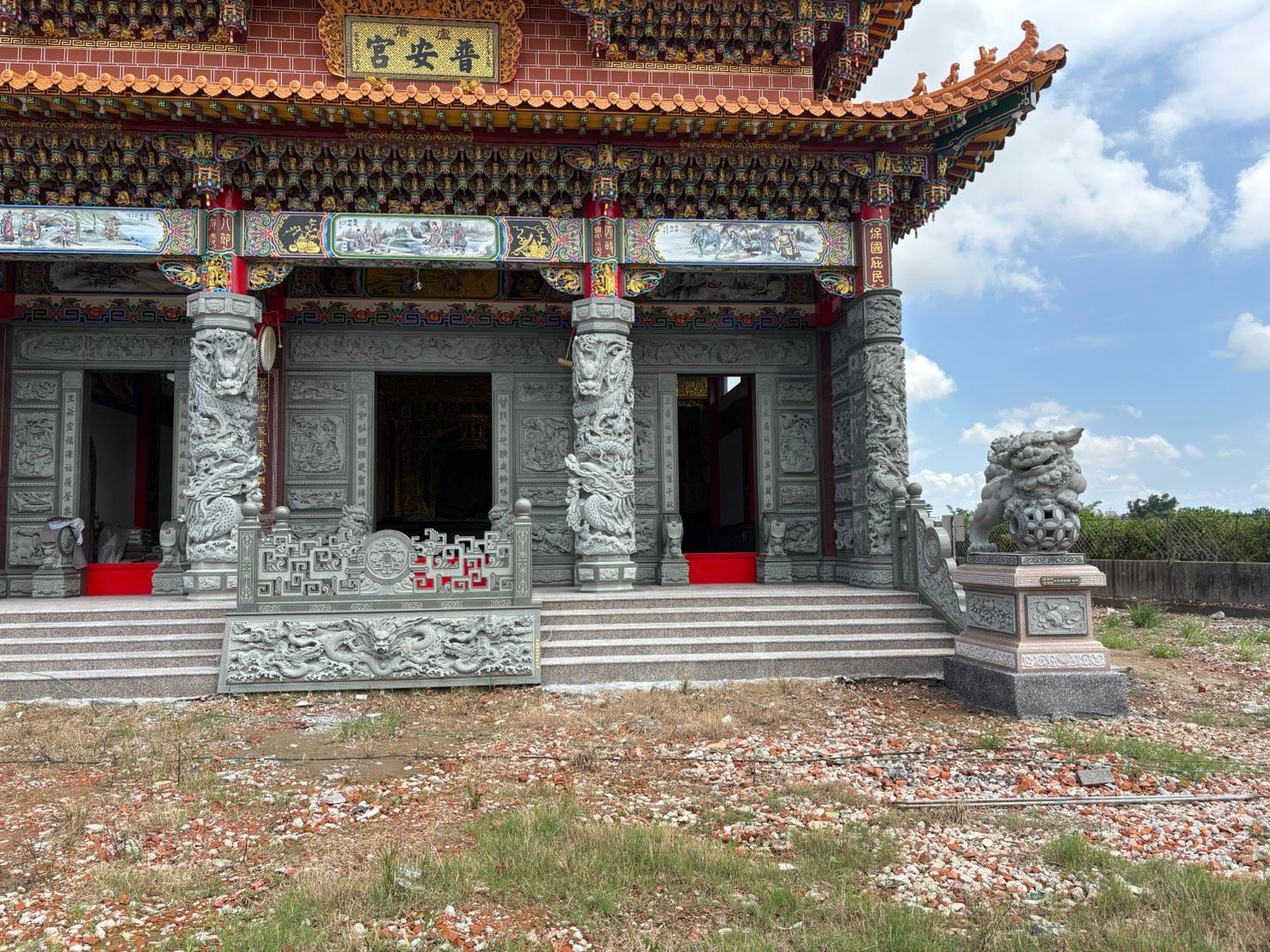 在晴朗的天空下,裝飾華麗的寺廟入口處有石柱、紅色大門和獅子雕像。