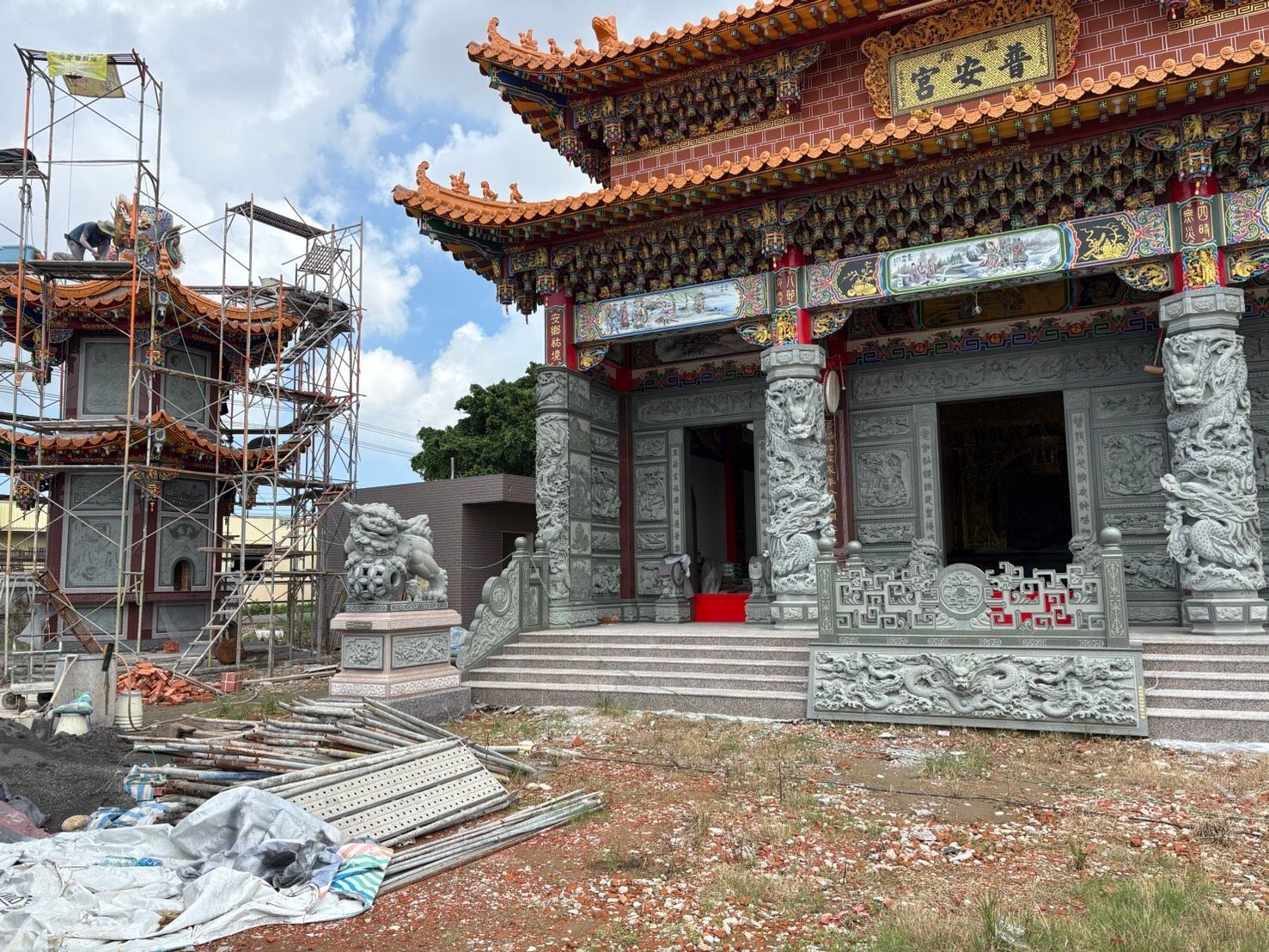一座屋頂裝飾華麗、石砌外牆的寺廟,旁邊搭著正在施工的鷹架,前方散落瓦礫。